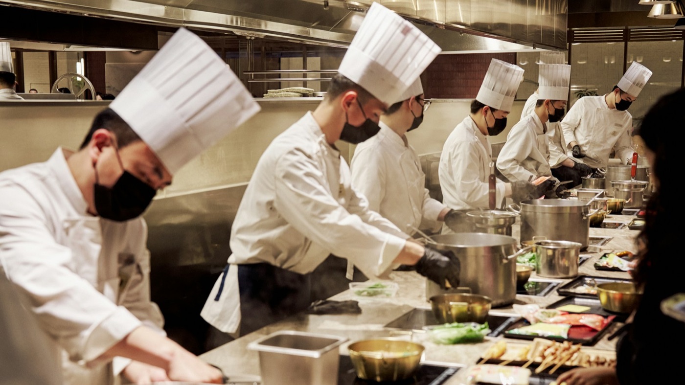 Brigade au travail dans une cuisine professionnelle, en toque, masque et gants